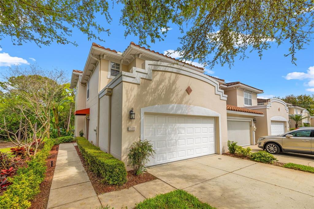 A two-story beige townhouse with a white garage door, tile roof, and landscaped walkway — 252 VALENCIA CIRCLE, ST PETERSBURG, FL