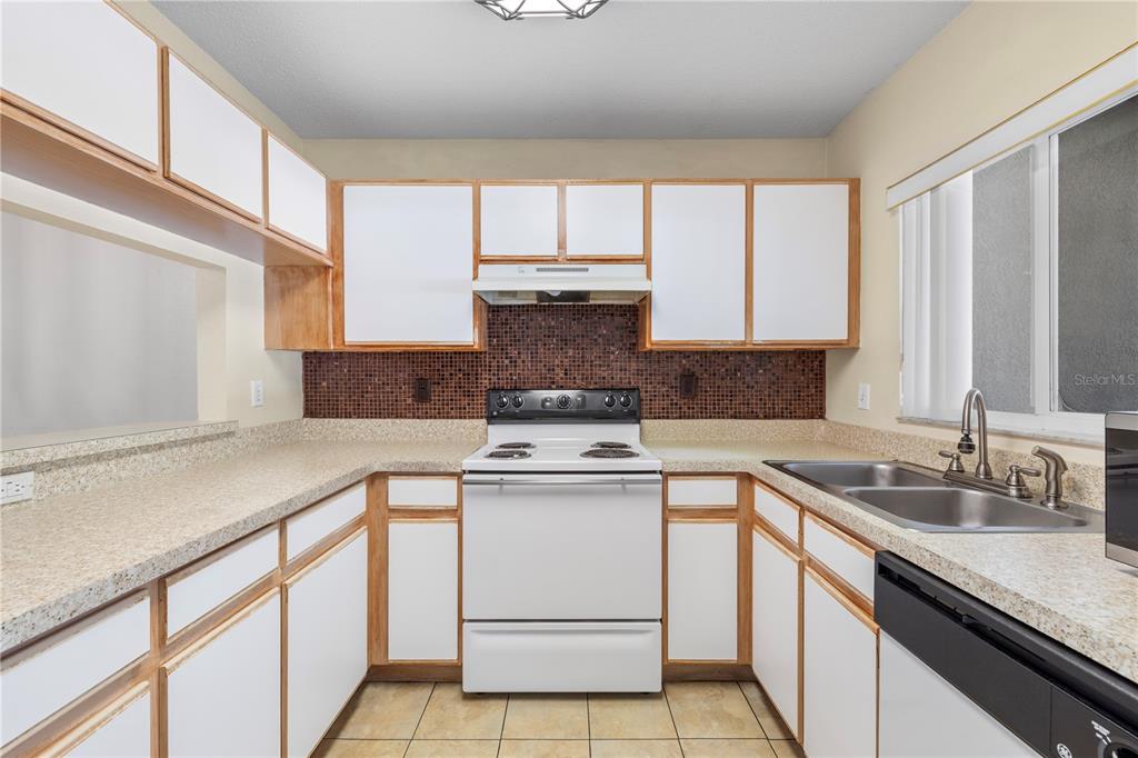 A kitchen with white cabinets, wood trim, a brown tiled backsplash, and white appliances — 1907 FLUORSHIRE DRIVE, BRANDON, FL