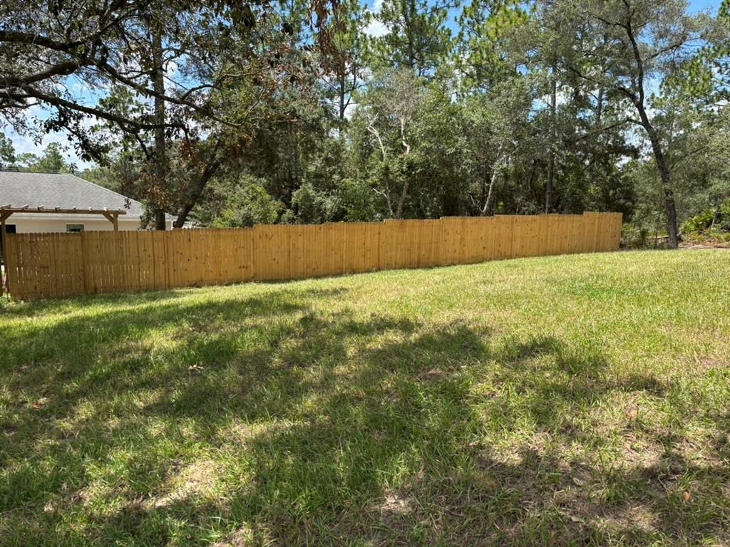 A wooden privacy fence borders a grassy backyard with trees in the background — 1808 W LINDEN DRIVE, DUNNELLON, FL
