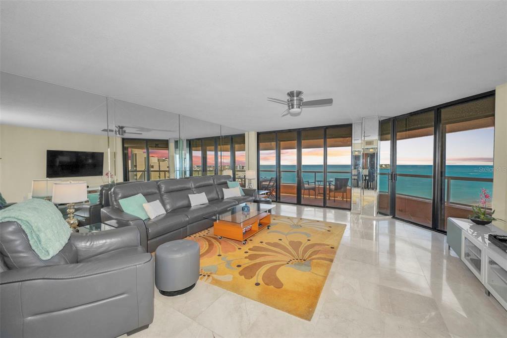 A living room with gray leather furniture, a yellow floral rug, and floor-to-ceiling ocean views — 1310 GULF BOULEVARD UNIT Penthouse A, CLEARWATER BEACH, FL