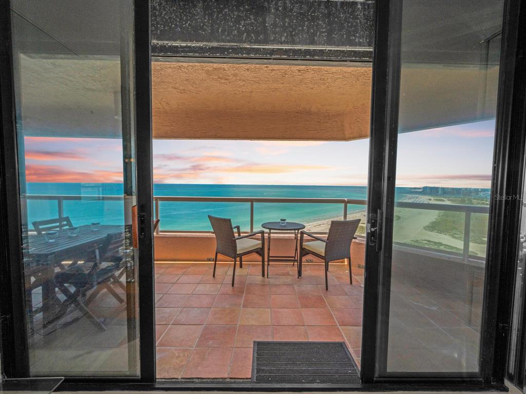 A balcony with tile flooring and patio furniture overlooks the ocean at sunset — 1310 GULF BOULEVARD UNIT Penthouse A, CLEARWATER BEACH, FL