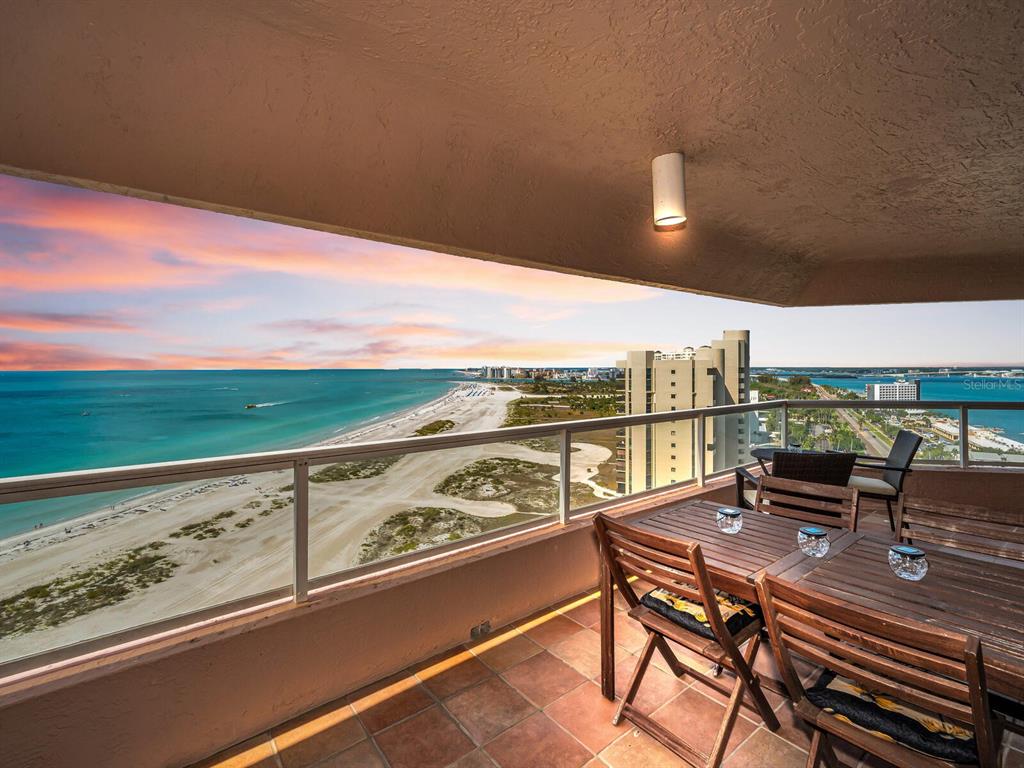 A balcony with a wooden dining set overlooks a sandy beach and the ocean — 1310 GULF BOULEVARD UNIT Penthouse A, CLEARWATER BEACH, FL