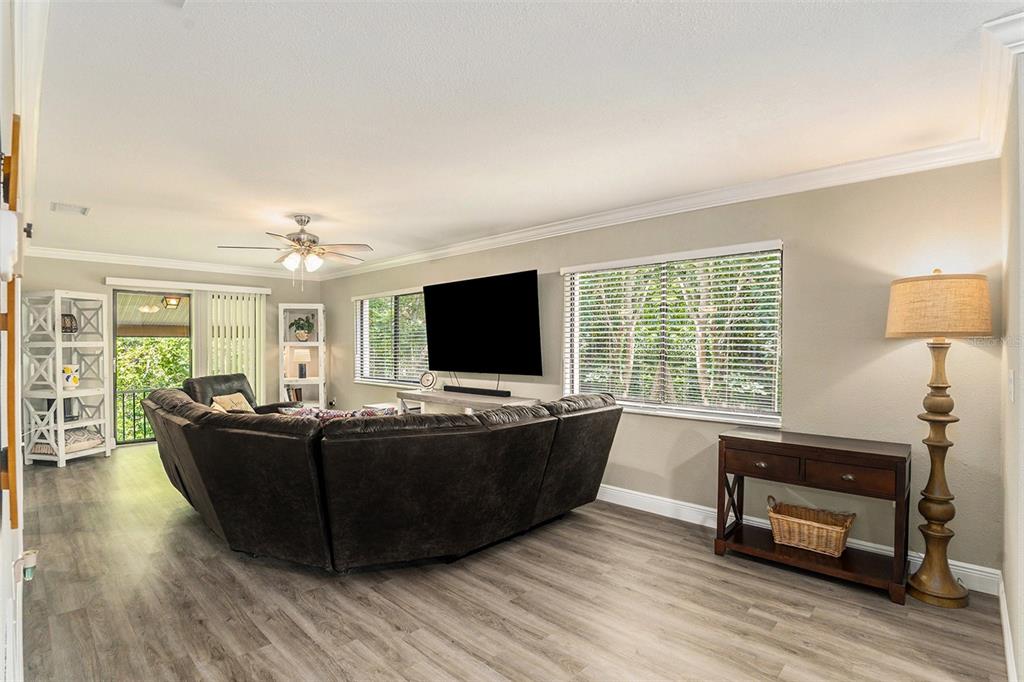 A living room features a dark sectional sofa, a wall-mounted television, and wood-look flooring — 12308 EAGLESWOOD DRIVE UNIT D, HUDSON, FL