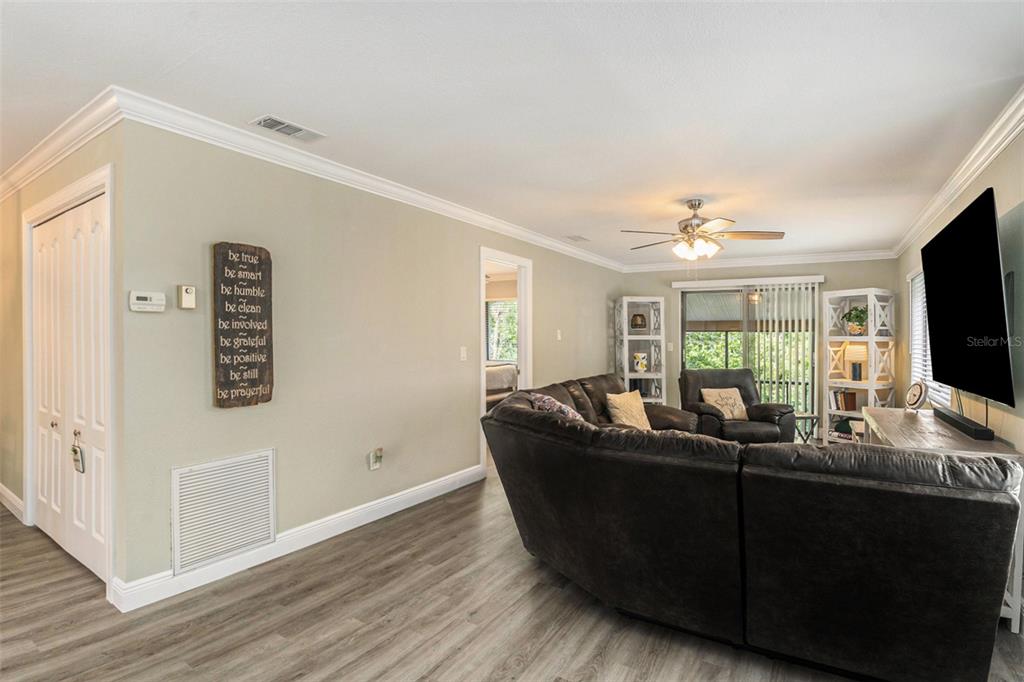 A living room features gray wood-look flooring, a large dark sofa, and a wall-mounted television — 12308 EAGLESWOOD DRIVE UNIT D, HUDSON, FL