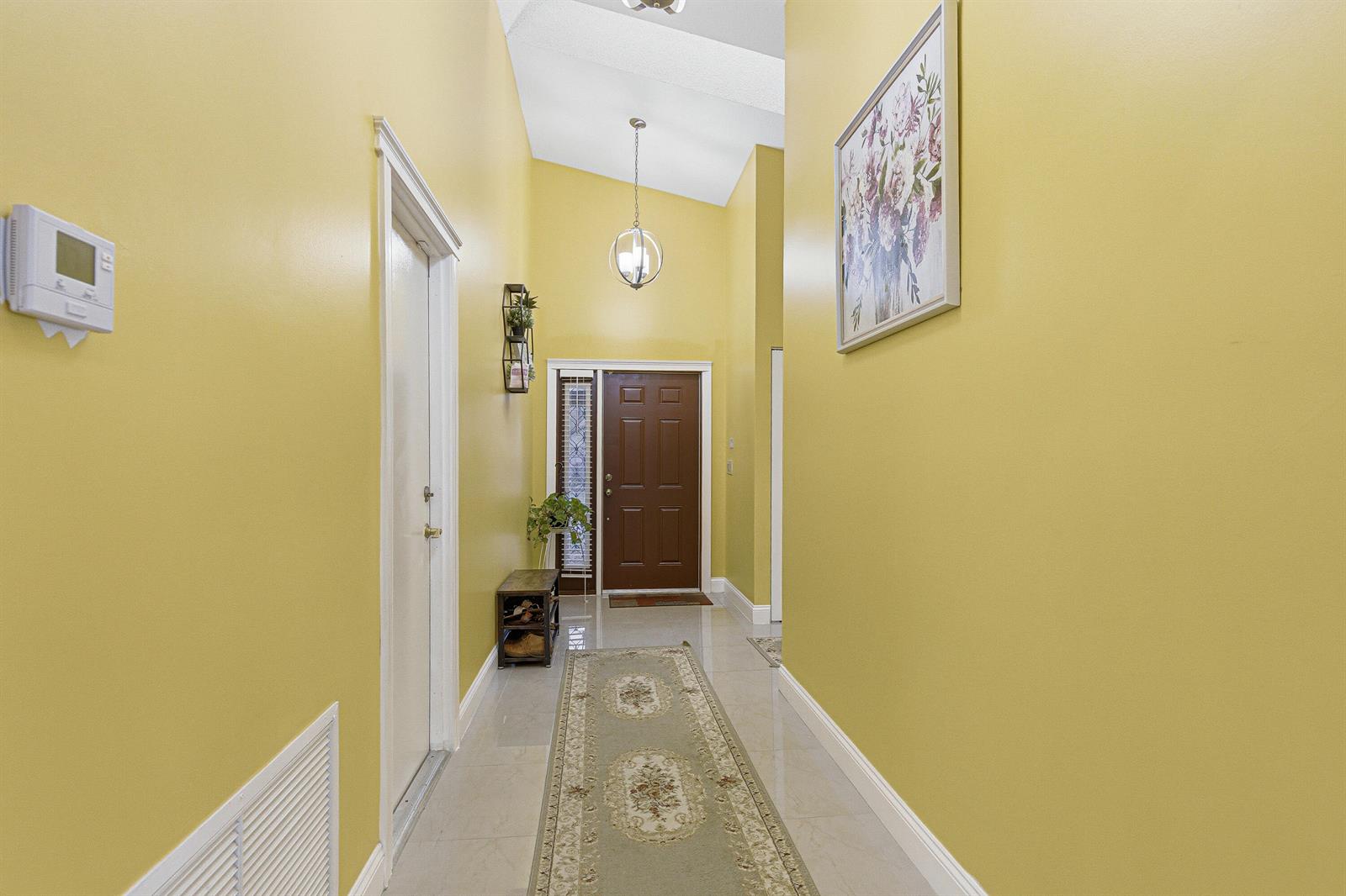 A yellow-walled entryway features a vaulted ceiling, tile flooring, a runner rug, and a door — 7040 Golf Pointe Circle, Tamarac FL 33321, TAMARAC, FL
