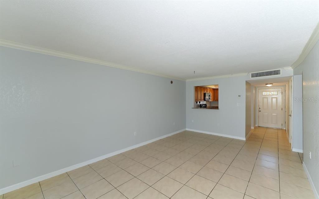 An open living area with light-colored tile flooring and a view into the kitchen — 942 LA COSTA CIRCLE UNIT 9, SARASOTA, FL