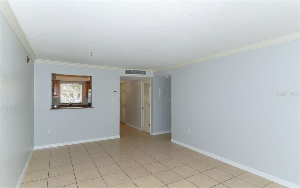 A living room with light-colored tile flooring and a pass-through window to the kitchen — 942 LA COSTA CIRCLE UNIT 9, SARASOTA, FL