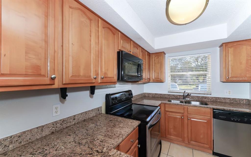 A kitchen with light wood cabinets, granite countertops, black appliances, and a window above the sink — 942 LA COSTA CIRCLE UNIT 9, SARASOTA, FL