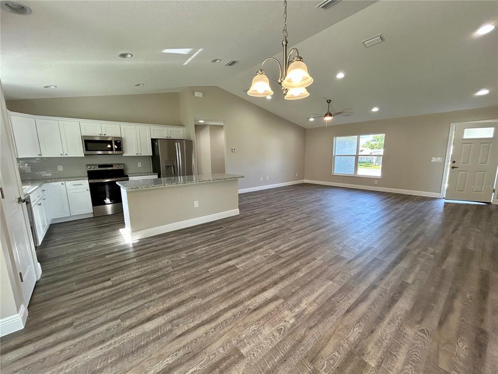 An open-concept kitchen and living area with white cabinets, stainless appliances, and wood-look flooring — 15625 SE 84TH TERRACE, SUMMERFIELD, FL