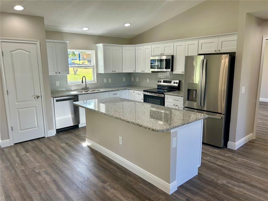 A kitchen features white cabinets, granite countertops, stainless steel appliances, and a central island — 15625 SE 84TH TERRACE, SUMMERFIELD, FL
