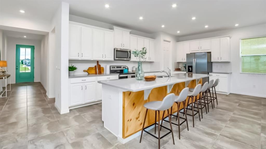 A modern kitchen features white cabinets, a large island with wood paneling, and gray tile flooring — 8962 HILTON RIDGE AVENUE, KISSIMMEE, FL