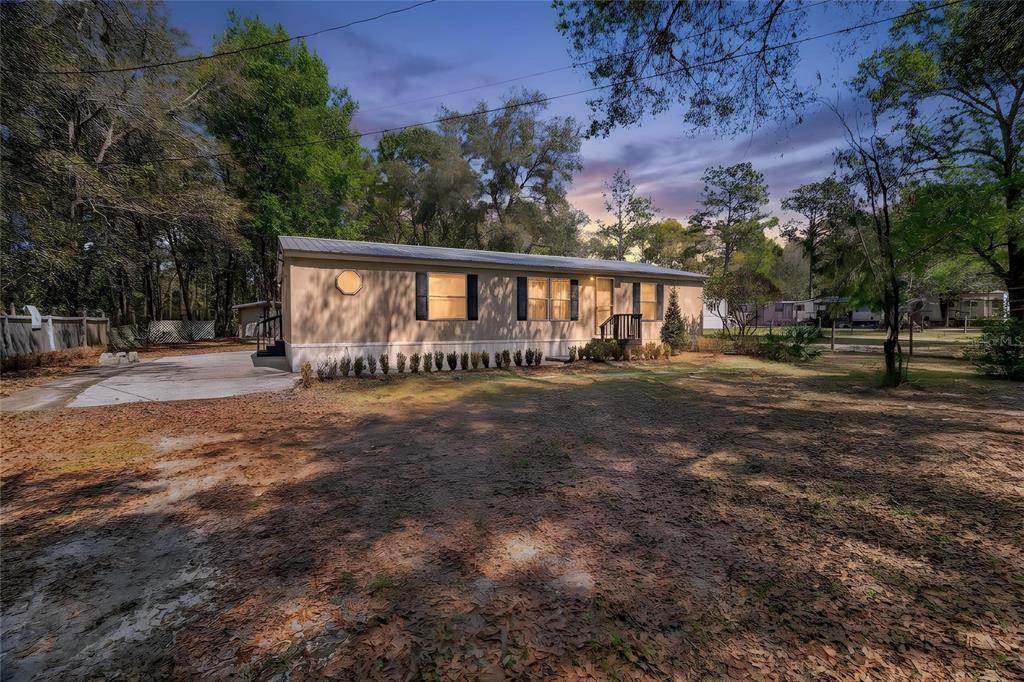 A single-story manufactured home with a metal roof sits on a wooded, dirt-covered lot — 14395 NE 50TH PLACE, WILLISTON, FL