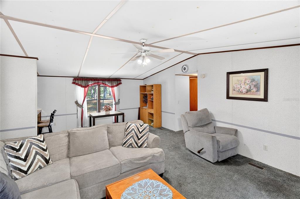 A living room features gray carpet, a sectional sofa, a recliner, and a ceiling fan — 14395 NE 50TH PLACE, WILLISTON, FL