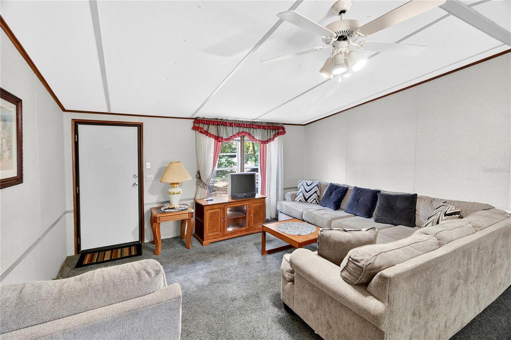 A living room features gray carpeting, a sectional sofa, a ceiling fan, and a television — 14395 NE 50TH PLACE, WILLISTON, FL