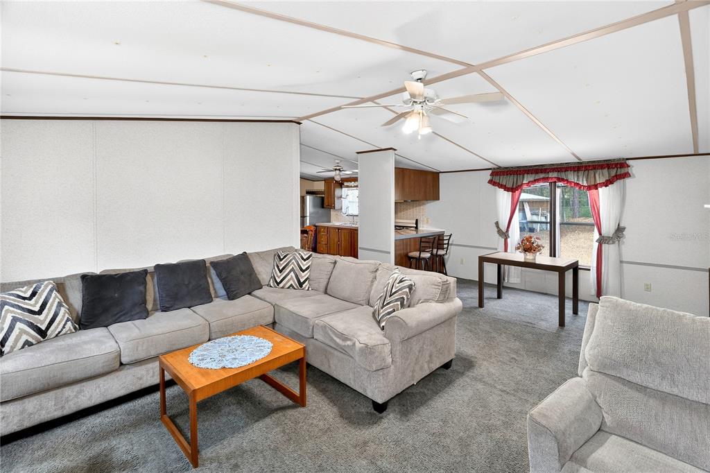 A living room with gray carpet, a large sectional sofa, and an open kitchen area — 14395 NE 50TH PLACE, WILLISTON, FL