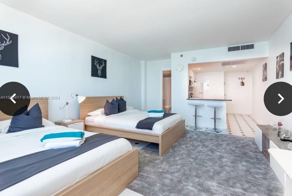 A hotel-style room features two beds, a gray area rug, and a small kitchen bar — 5445 Collins Ave # 1135, Miami Beach FL 33140, MIAMI BEACH, FL