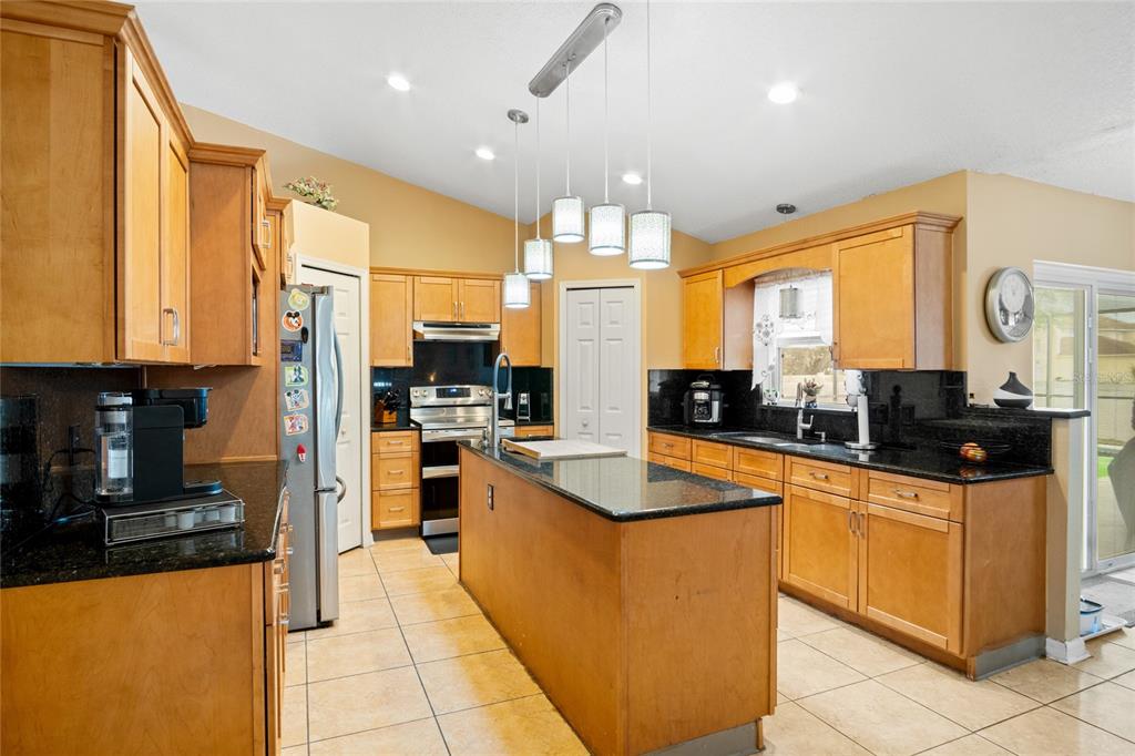 A kitchen features light wood cabinets, black granite countertops, a center island, and tile flooring — 203 FLOUNDER PLACE, POINCIANA, FL