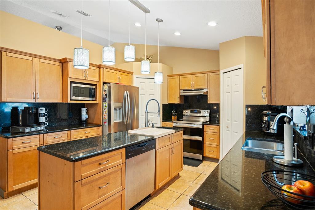 A kitchen features light wood cabinets, black granite countertops, stainless steel appliances, and pendant lighting — 203 FLOUNDER PLACE, POINCIANA, FL