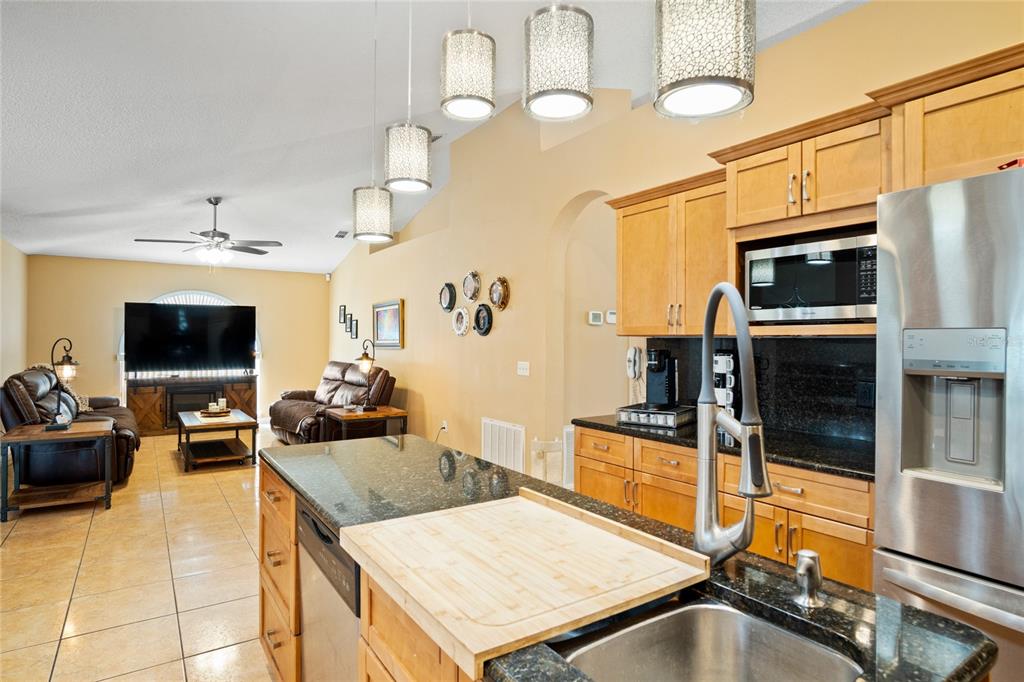 A kitchen with granite countertops and wood cabinets overlooks an open-concept living room — 203 FLOUNDER PLACE, POINCIANA, FL