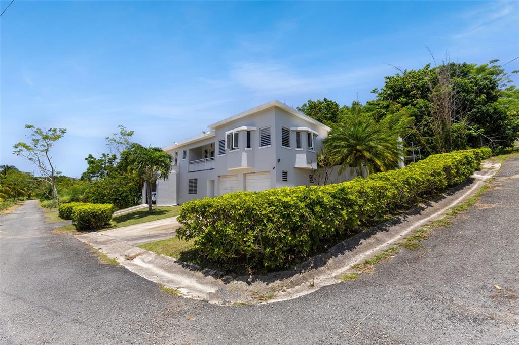 A two-story light gray house features a manicured hedge and a paved driveway — Lote 30 BARRIO ENSENADA, RINCON, PR