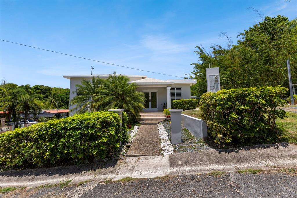 A single-story house with a white exterior, a central walkway, and lush landscaping — Lote 30 BARRIO ENSENADA, RINCON, PR