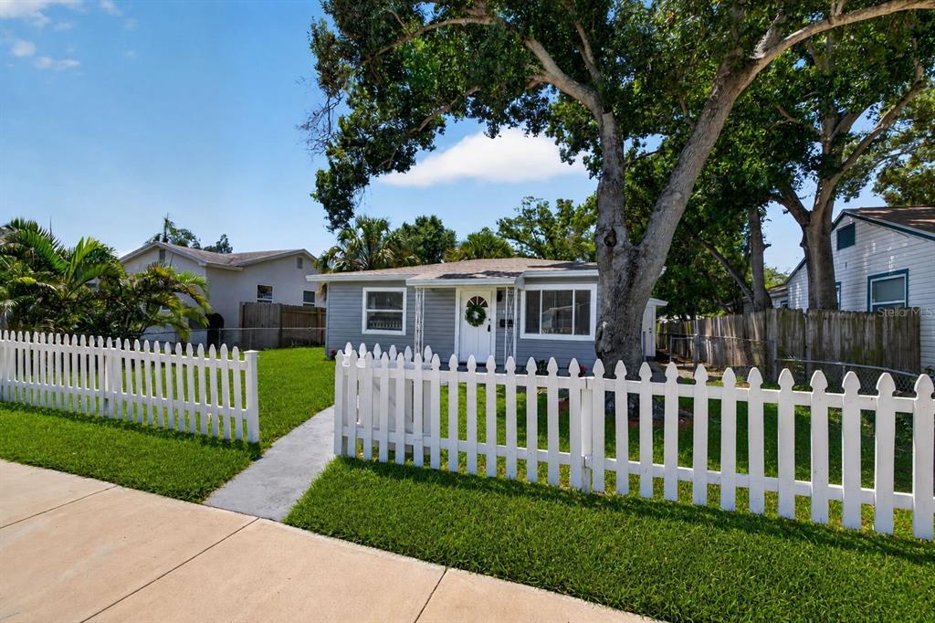 A single-story gray house with a white picket fence and a large tree in front — 4110 3RD AVENUE S, ST PETERSBURG, FL