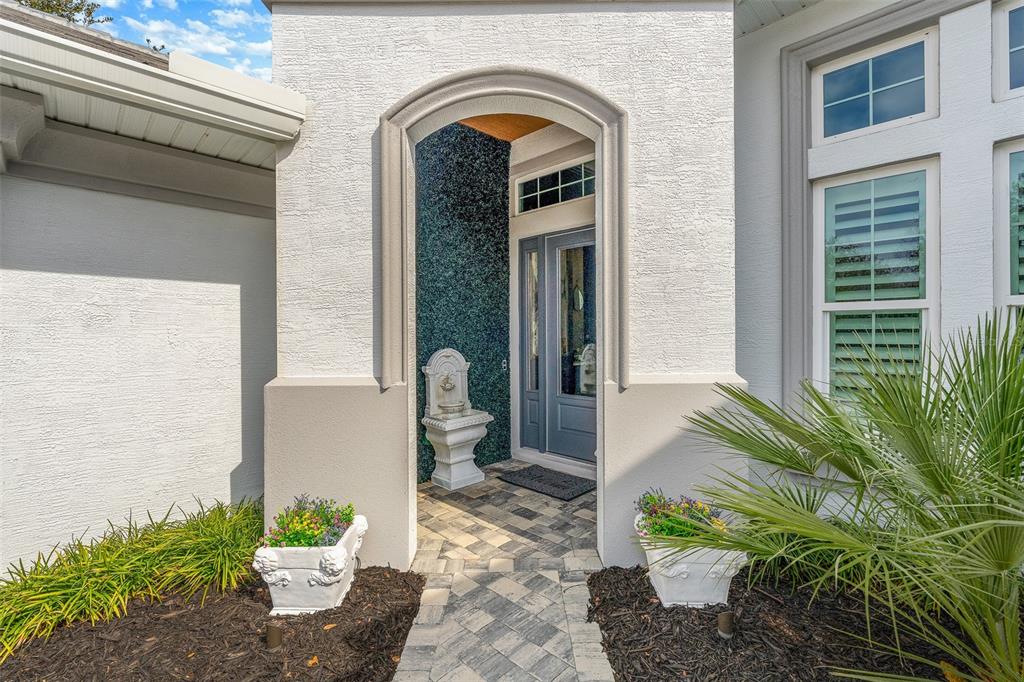 A white stucco entryway features a stone fountain, a blue door, and two white planters — 241 CONSERVATORY DRIVE, PALM COAST, FL
