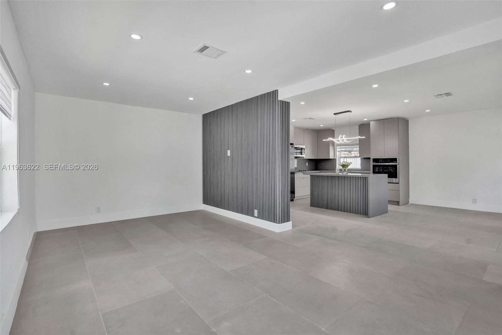 A modern, open-concept living area features large gray floor tiles and a slatted accent wall — 1010 N 16th Ave, Hollywood FL 33020, HOLLYWOOD, FL