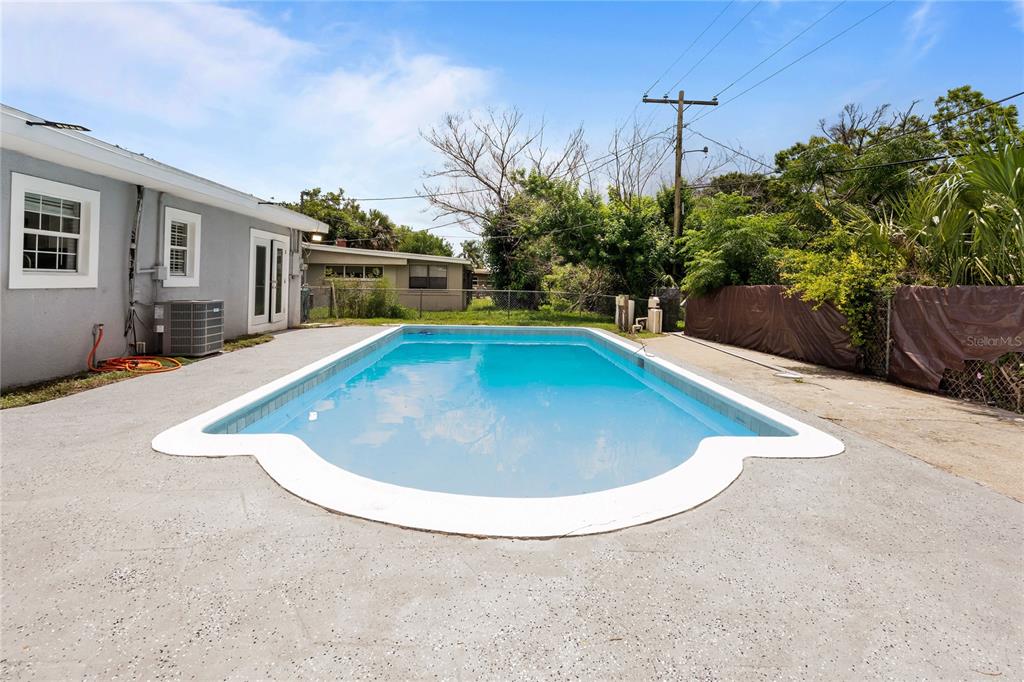A rectangular swimming pool with a curved edge sits on a concrete patio behind a house — 815 W HIGHLAND DRIVE, COCOA, FL
