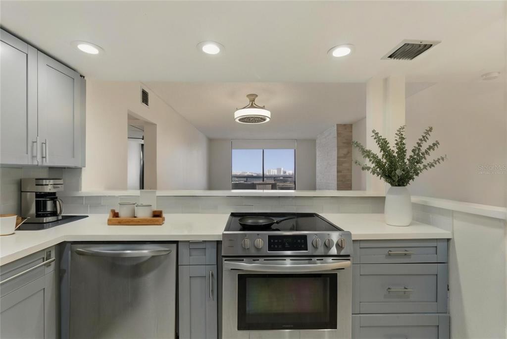 A kitchen with gray cabinets, stainless steel appliances, and a pass-through window to the living area — 500 THREE ISLANDS BOULEVARD UNIT 1008, HALLANDALE BEACH, FL