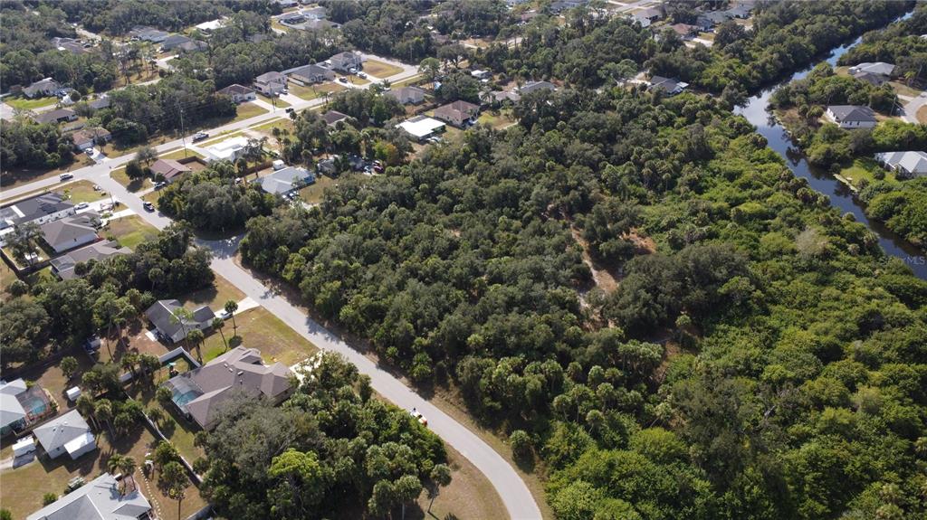 An aerial view shows a wooded vacant lot situated between a residential street and water — ALFA TERRACE, NORTH PORT, FL
