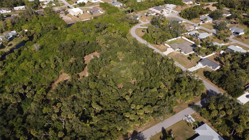 An aerial view shows a wooded, undeveloped lot surrounded by residential houses and paved streets — ALFA TERRACE, NORTH PORT, FL