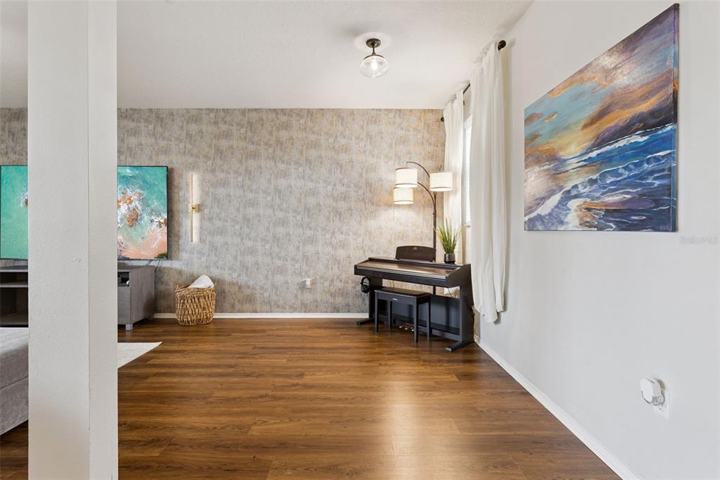 A living room features wood-look flooring, a textured accent wall, a piano, and wall art — 13537 LARANJA STREET, CLERMONT, FL