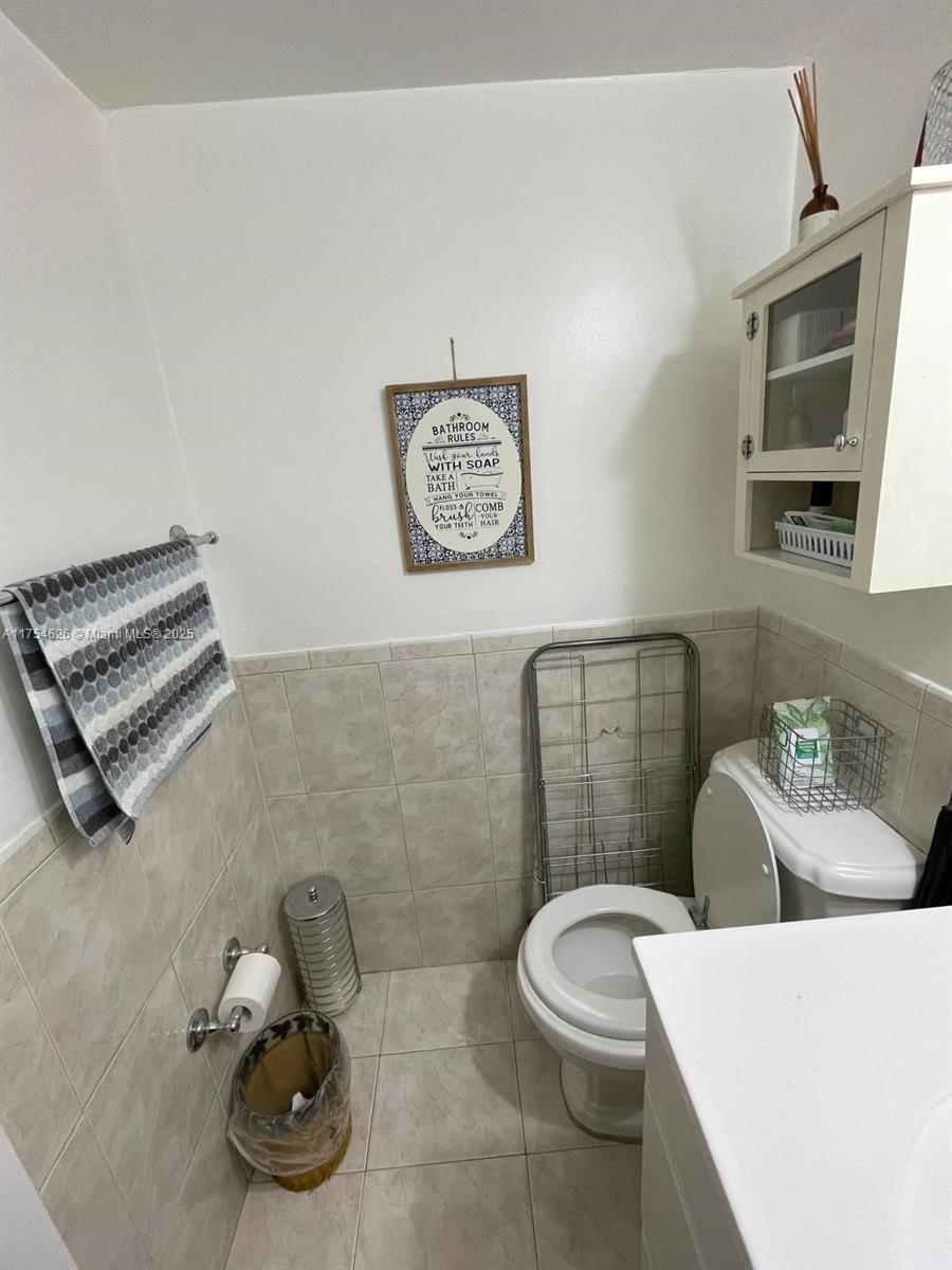 A small bathroom features beige tiled walls, a toilet, a wall-mounted cabinet, and a towel rack — 10985 SW 107th St # 211, Miami FL 33176, MIAMI, FL