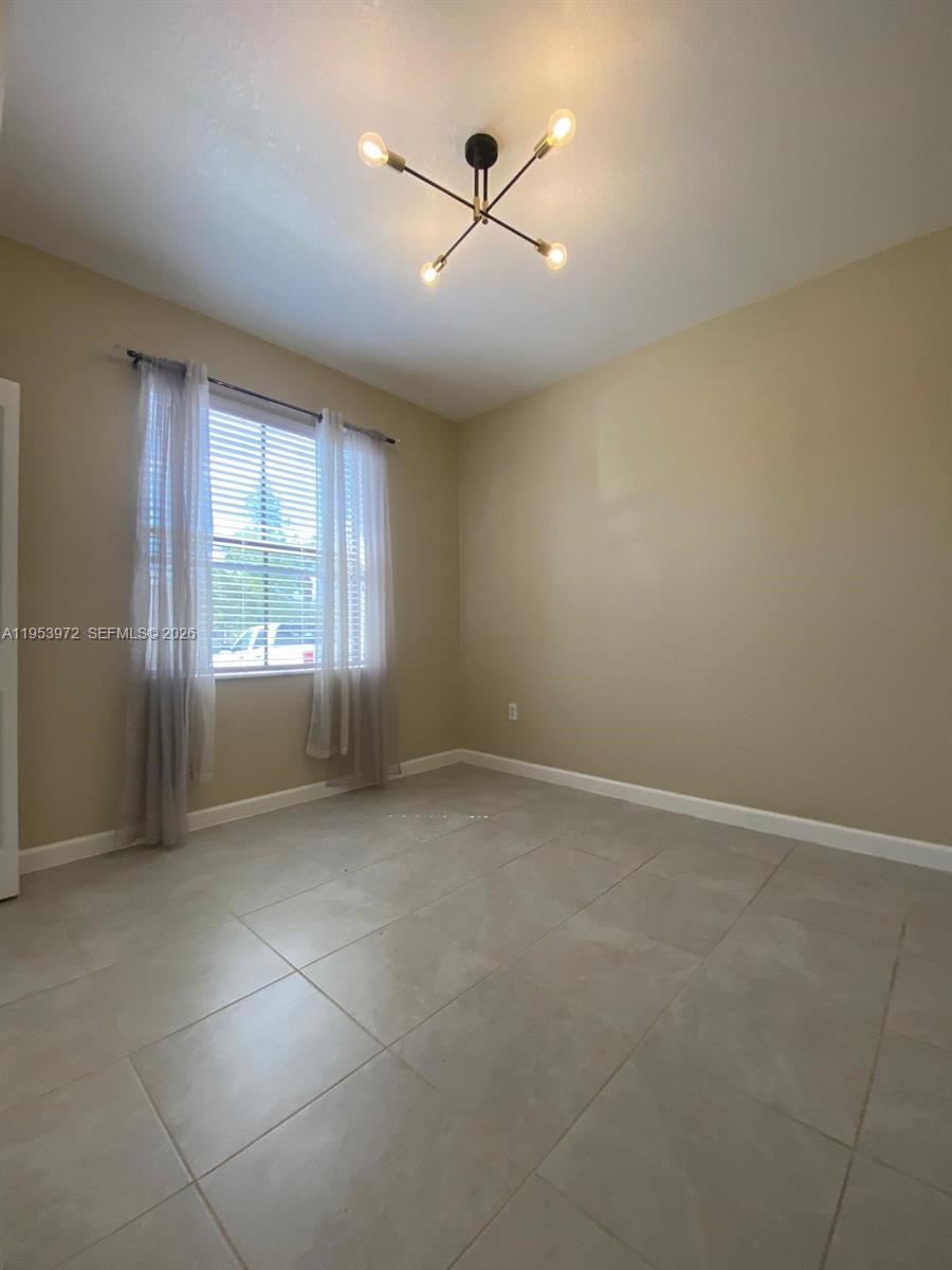 An empty room features beige walls, large light-colored floor tiles, and a modern ceiling light — 18220 SW 148th Rd, Miami FL 33187, MIAMI, FL