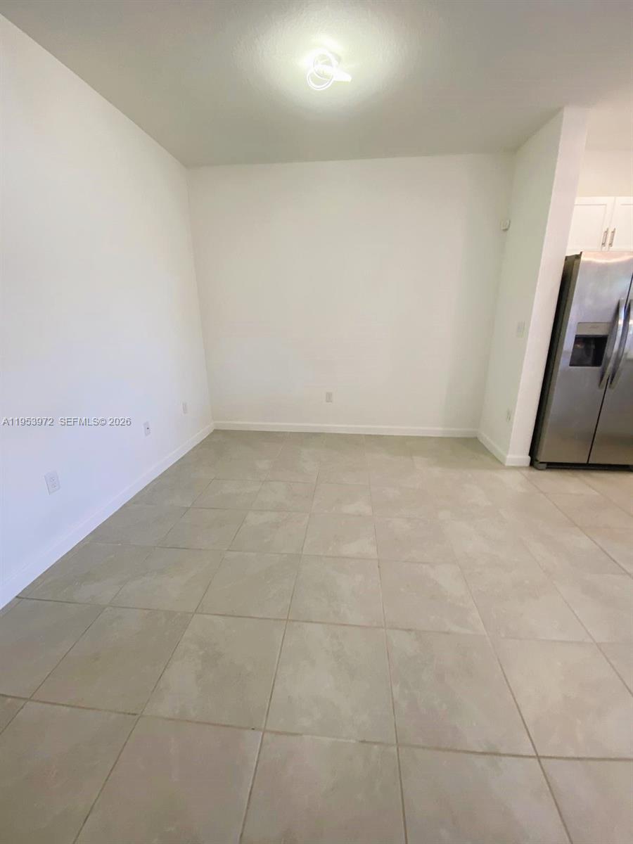 This room features light-colored tile flooring, white walls, and an adjacent stainless steel refrigerator — 18220 SW 148th Rd, Miami FL 33187, MIAMI, FL
