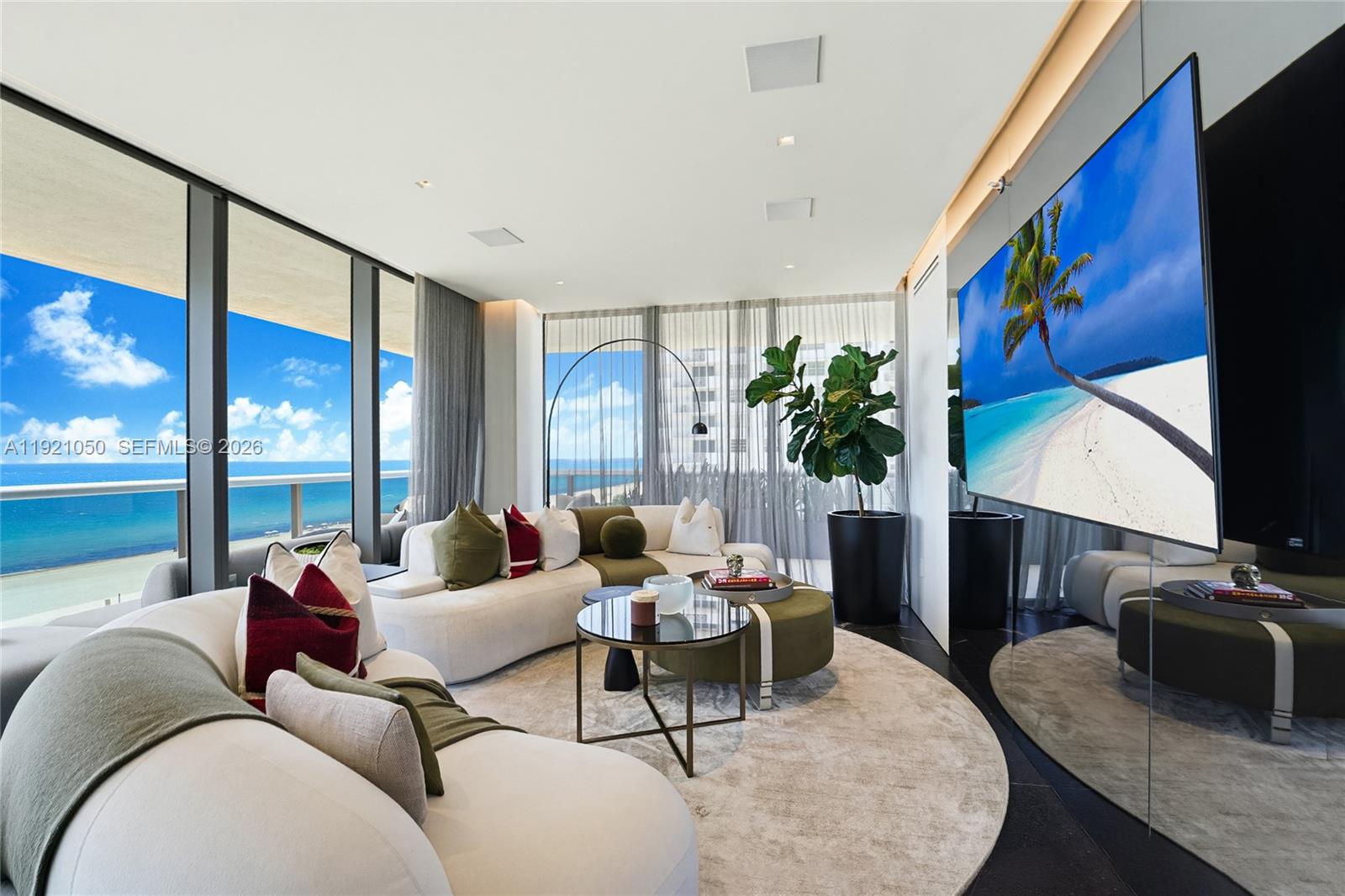 A modern living room features a curved white sofa, circular coffee table, and ocean views — 5875 Collins Ave # 902, Miami Beach FL 33140, MIAMI BEACH, FL