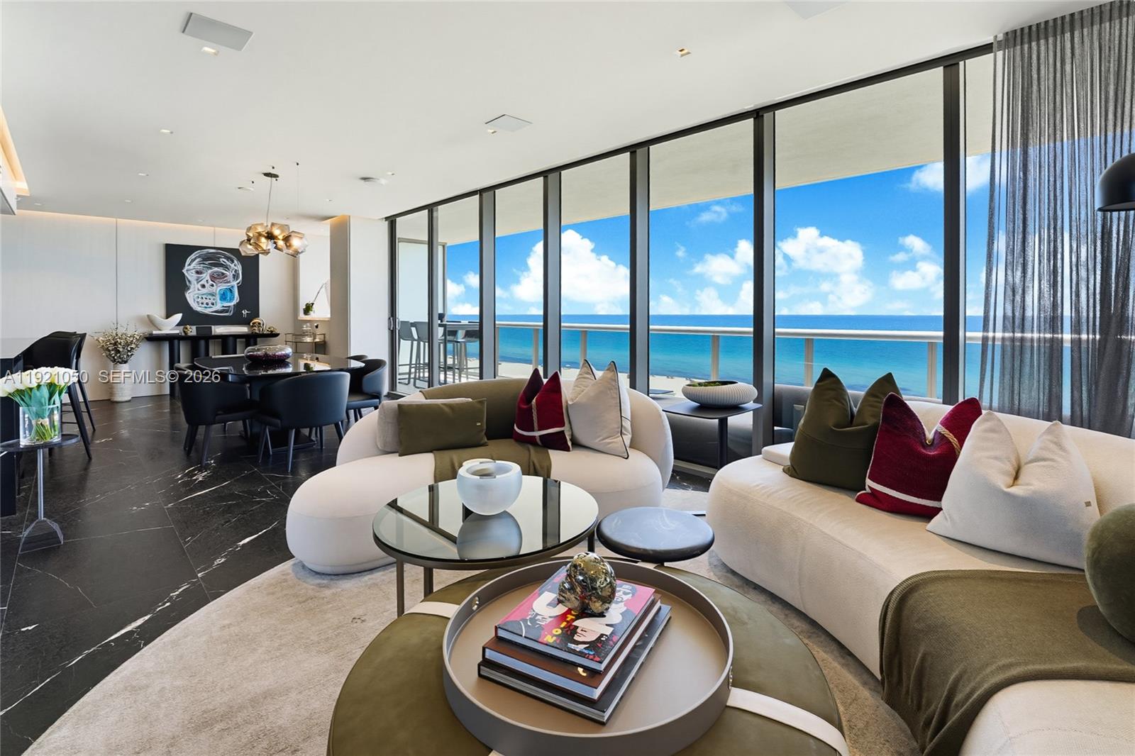 A modern living room with curved sofas, black marble floors, and floor-to-ceiling ocean views — 5875 Collins Ave # 902, Miami Beach FL 33140, MIAMI BEACH, FL