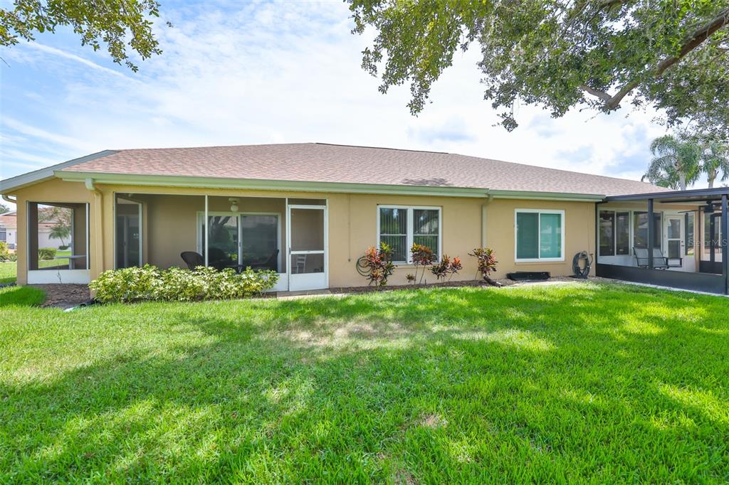 The back exterior of a tan house features a screened-in patio and a grassy yard — 751 MCCALLISTER AVENUE, SUN CITY CENTER, FL