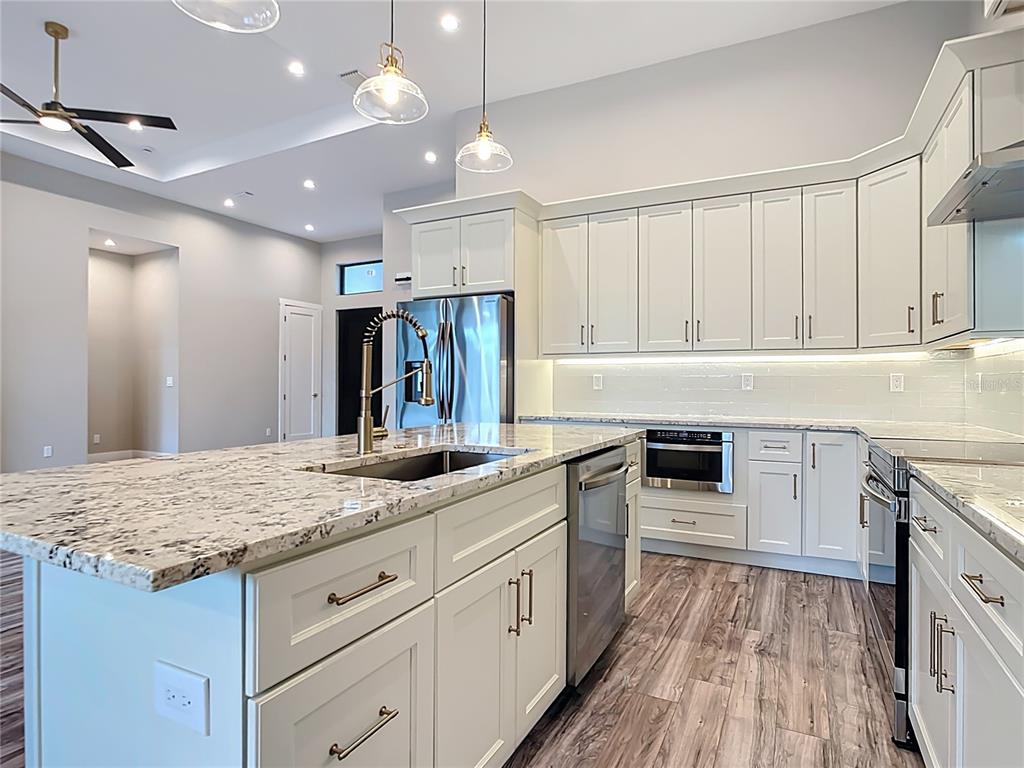 A modern kitchen features white cabinetry, granite countertops, a large island, and stainless steel appliances — 7152 BOUGAINVILLEA STREET, ENGLEWOOD, FL
