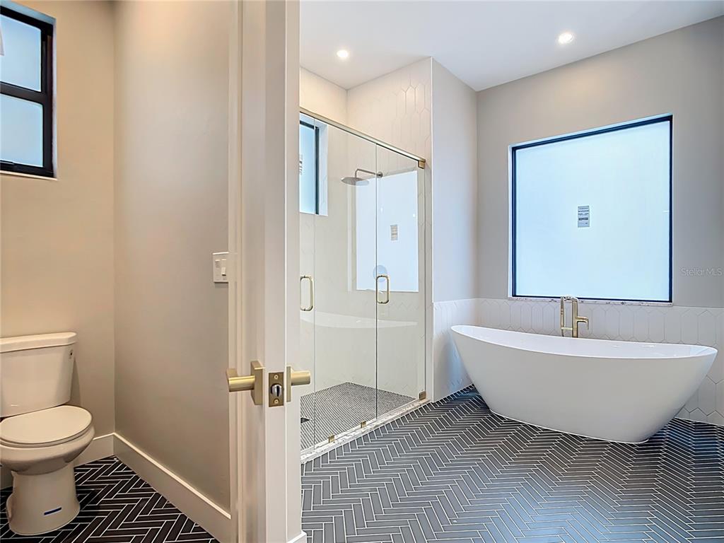 A bathroom features a freestanding tub, a glass-enclosed shower, and dark herringbone floor tiles — 7152 BOUGAINVILLEA STREET, ENGLEWOOD, FL