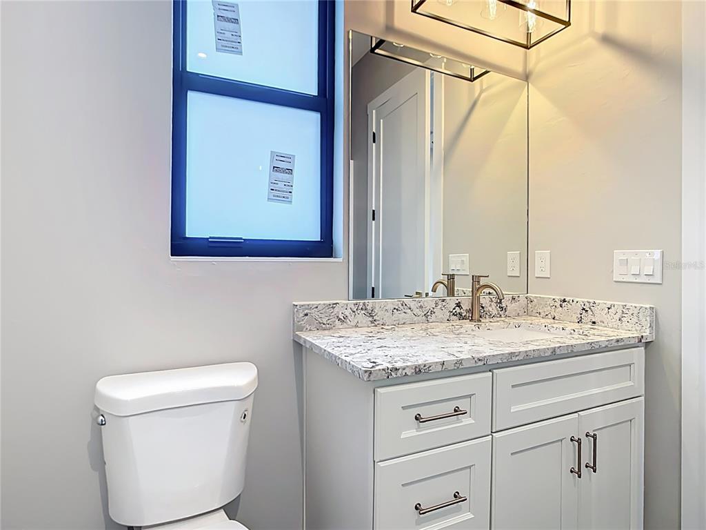 A bathroom features a white vanity with a granite countertop, a mirror, and a toilet — 7152 BOUGAINVILLEA STREET, ENGLEWOOD, FL