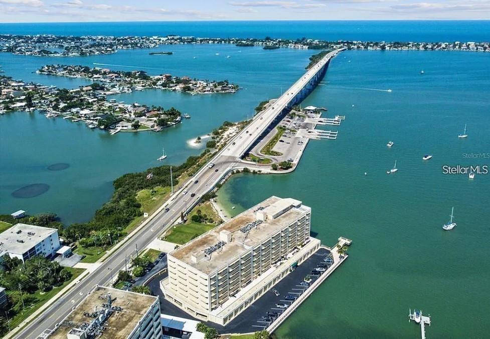 An aerial view shows a multi-story building, a long bridge, and surrounding water with boats — 100 BLUFF VIEW DRIVE UNIT 308A, BELLEAIR BLUFFS, FL