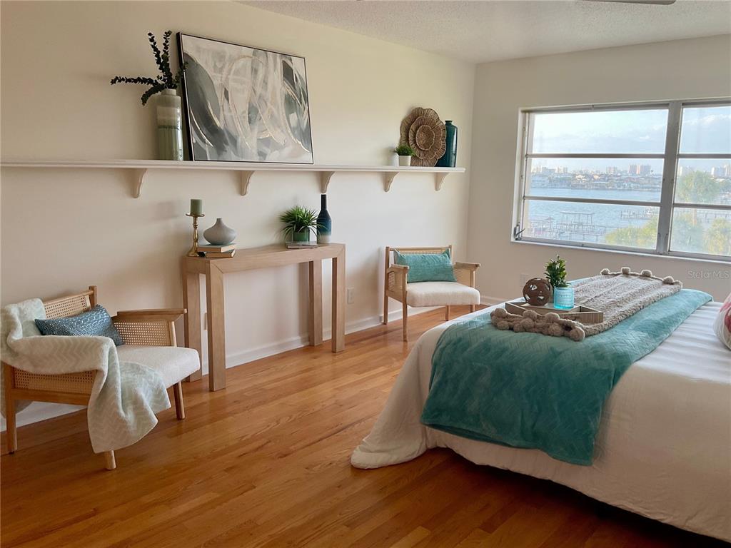 A bedroom features hardwood floors, a long wall shelf, two rattan chairs, and a water view — 100 BLUFF VIEW DRIVE UNIT 308A, BELLEAIR BLUFFS, FL