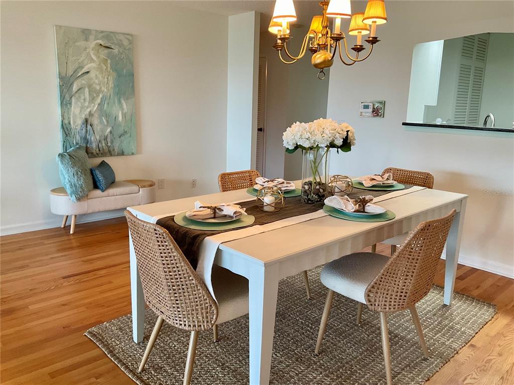 A dining room features a white table, woven chairs, a chandelier, and a heron painting — 100 BLUFF VIEW DRIVE UNIT 308A, BELLEAIR BLUFFS, FL