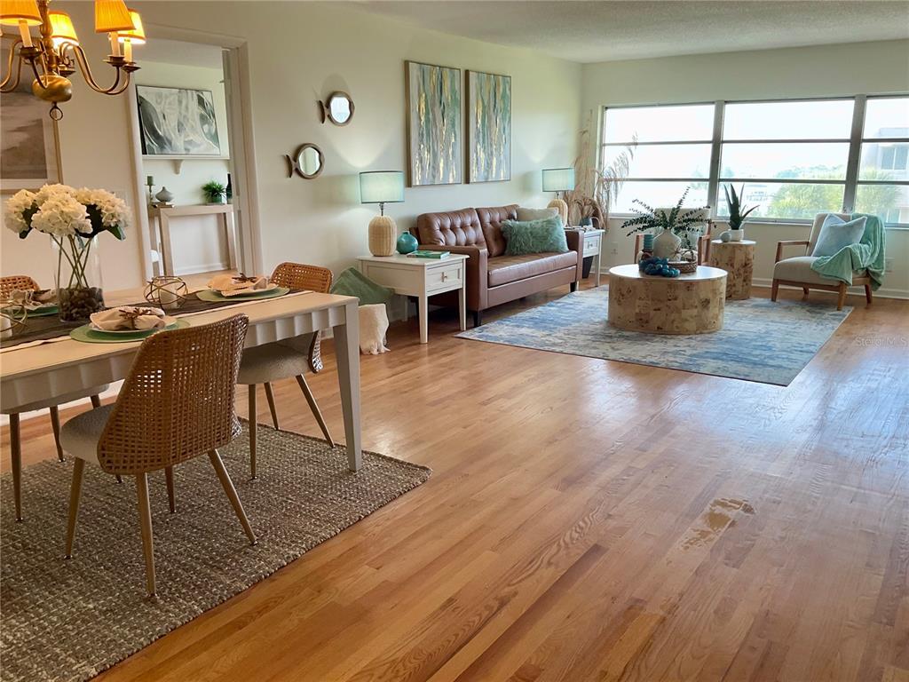 An open-concept living and dining area features hardwood floors, a leather sofa, and large windows — 100 BLUFF VIEW DRIVE UNIT 308A, BELLEAIR BLUFFS, FL