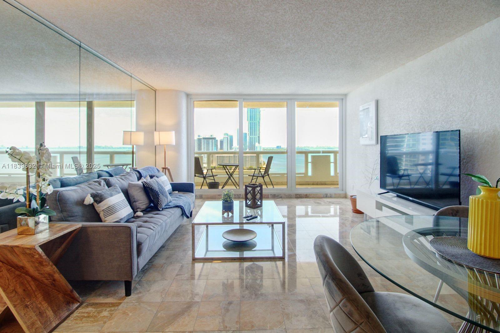 A living room features a grey sofa, glass coffee table, and a balcony with city views — 1717 N Bayshore Dr # 2635, Miami FL 33132, MIAMI, FL