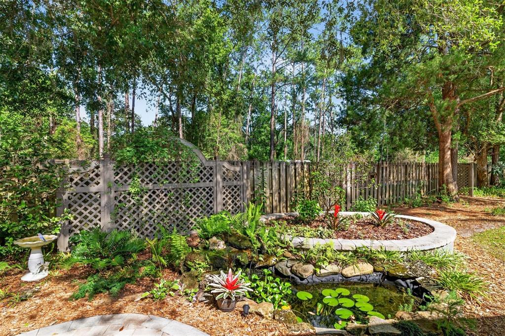 A backyard garden features a small stone pond, a raised planter bed, and wooden fencing — 2305 NW 44TH PLACE, GAINESVILLE, FL