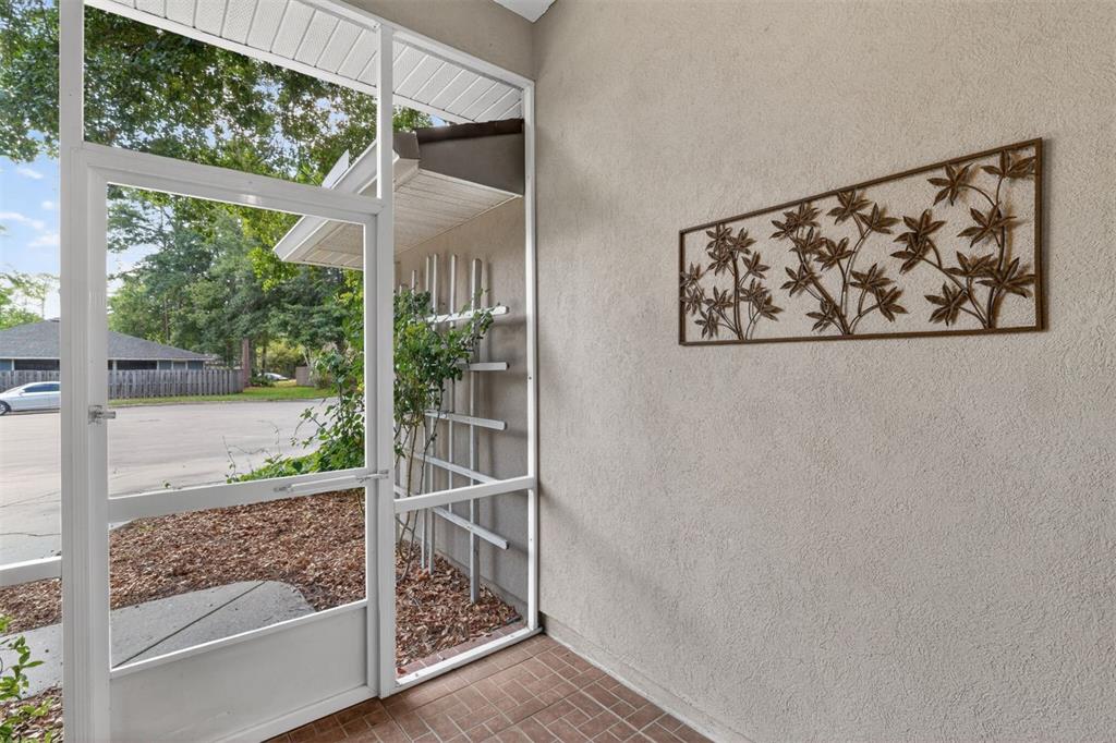 A screened-in porch features a tiled floor, a metal wall art piece, and a trellis — 2305 NW 44TH PLACE, GAINESVILLE, FL