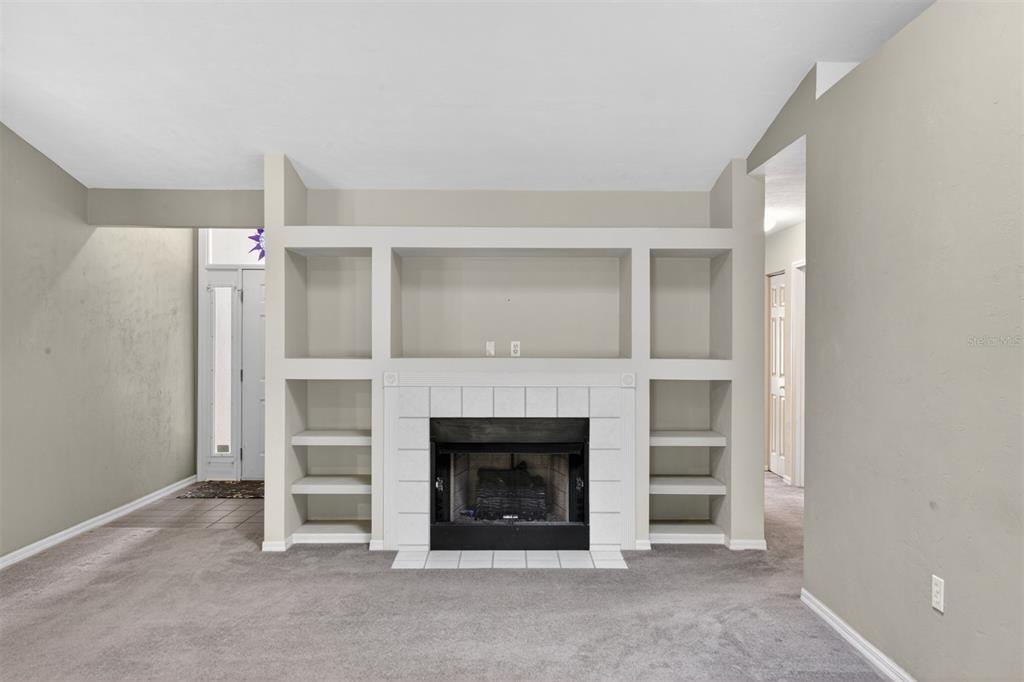A living room features a white tiled fireplace surrounded by built-in shelving and gray carpet — 2305 NW 44TH PLACE, GAINESVILLE, FL
